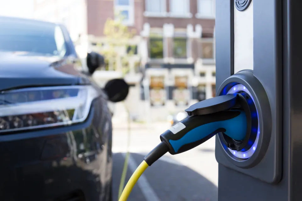 Close-up of electric car charging port with blurred dark colored car in background.